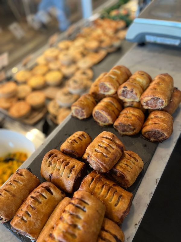 Bakery display of golden-brown pastries and sausage rolls on trays at a counter