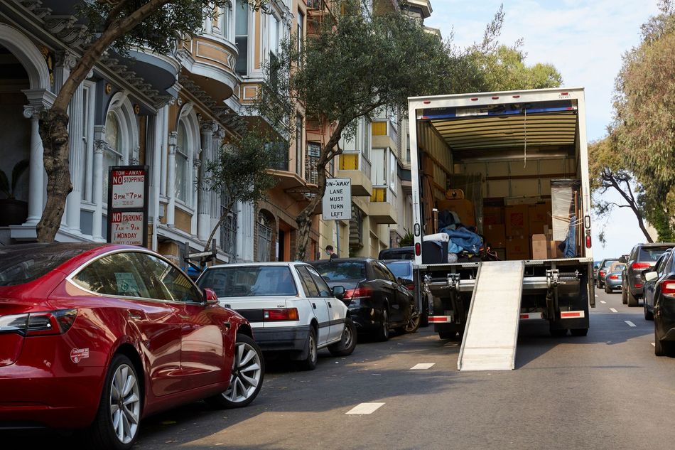 Moving truck with ramp parked on a tree-lined street beside parked cars and buildings Moving truck with ramp parked on a tree-lined street beside parked cars and buildings
