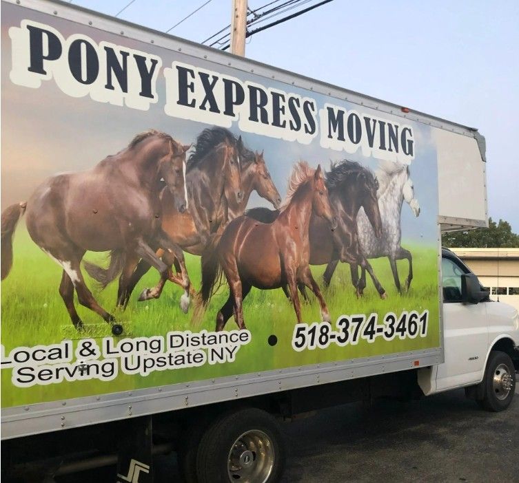 Piny Express MovinMovers loading cardboard boxes from a white van outside a modern buildingg truck parked in a driveway beside a house and black pickup truck. Movers loading cardboard boxes from a white van outside a modern building
