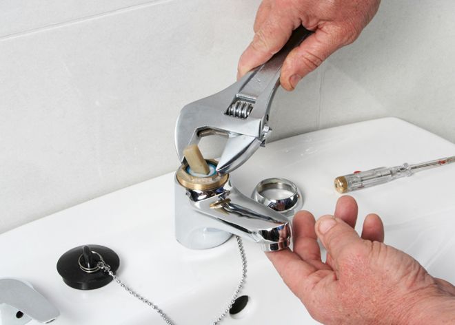 Hands using a wrench to loosen a bathroom sink drain assembly.