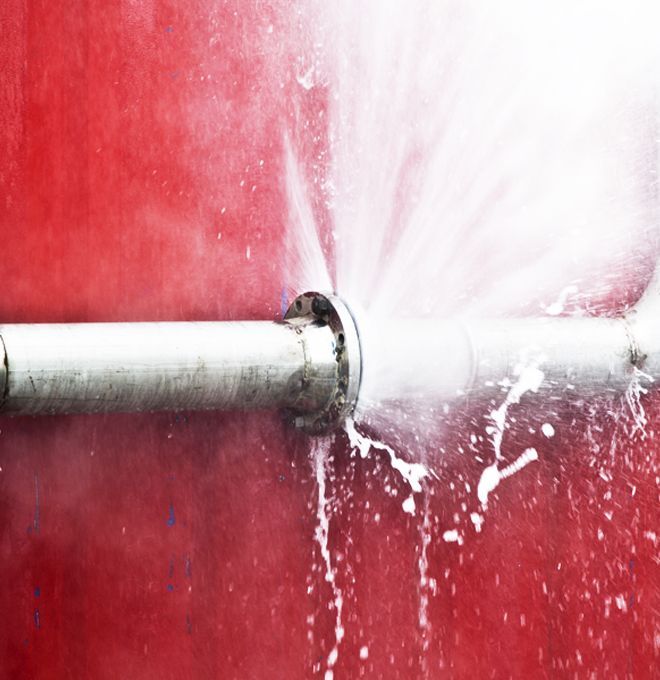 Bursting fire sprinkler spraying water against a red wall