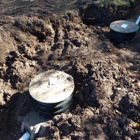 Two black utility access covers in muddy ground at a construction site