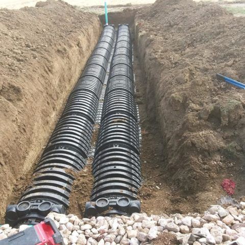 Two black corrugated drainage pipes laid in a trench, surrounded by dirt and rocks.