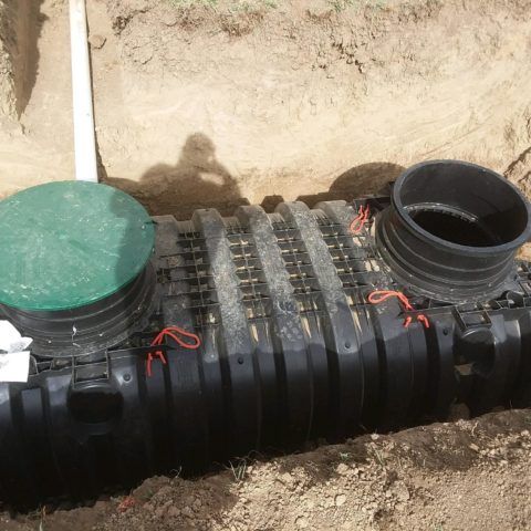 Black underground septic tank with green and open black lids in a dirt trench