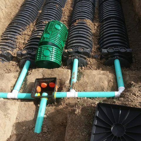 Underground drainage pipes with green and black corrugated chambers connected by light blue PVC pipes.