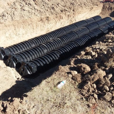 Black corrugated drainage pipes stacked on dirt at a construction site