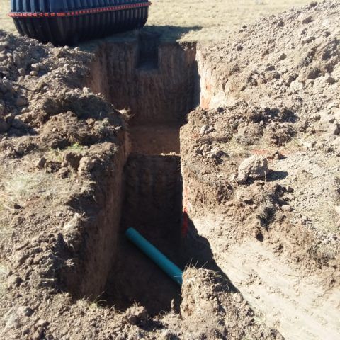 Excavated trench in dry soil with a blue pipe exposed near the bottom