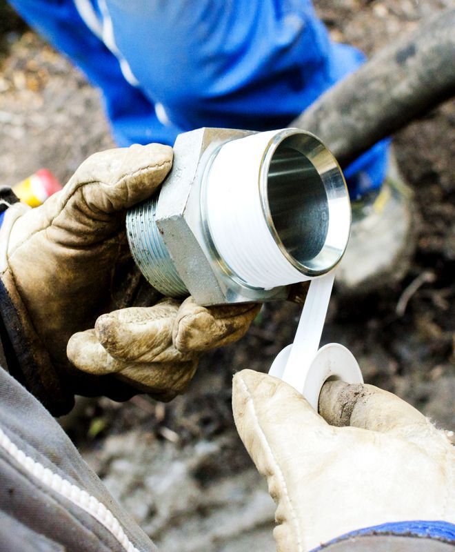 Gloved hands wrapping white plumber’s tape around a metal pipe fitting outdoors