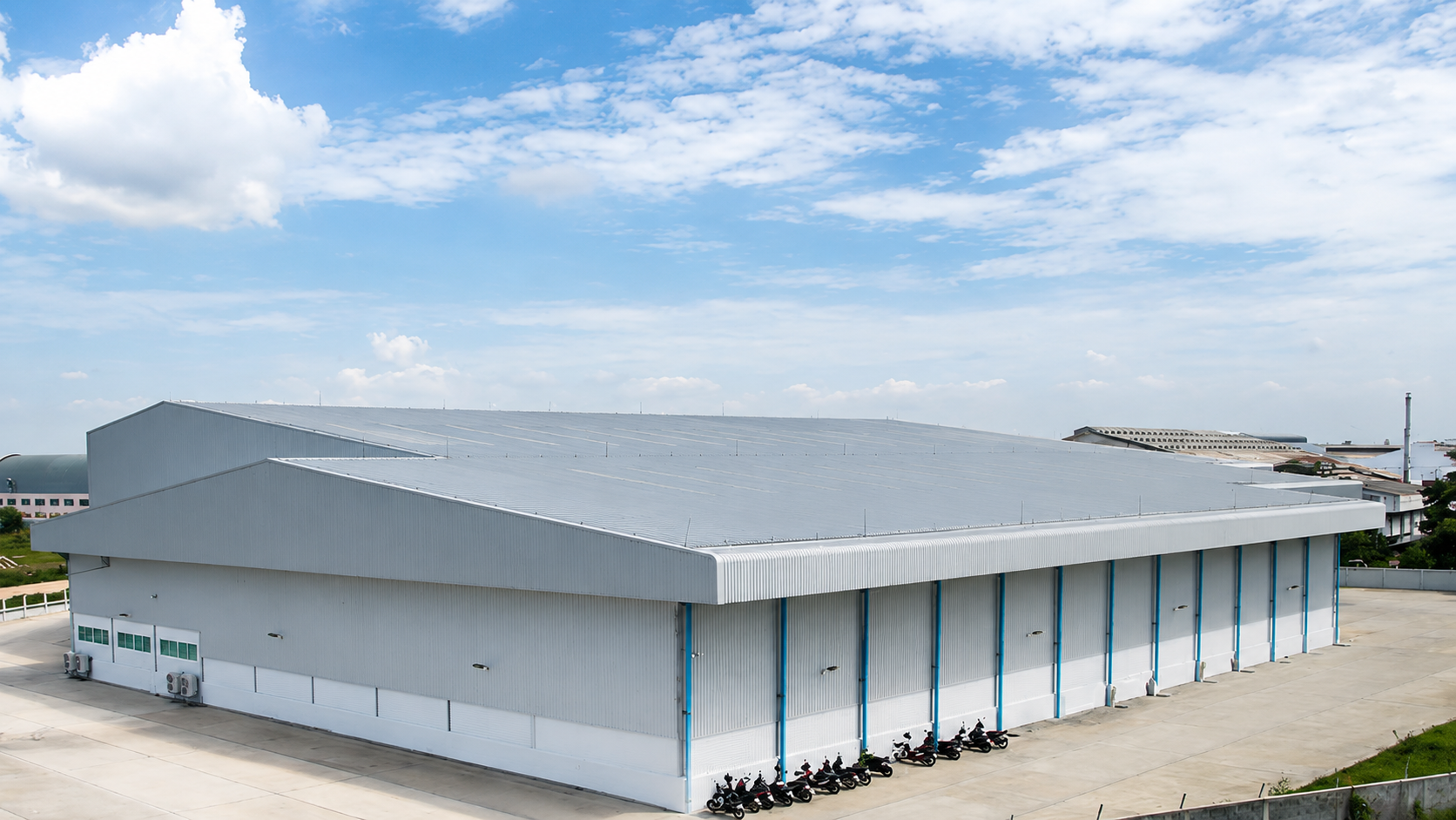 Large white warehouse with a gray roof in an open industrial area under a blue sky