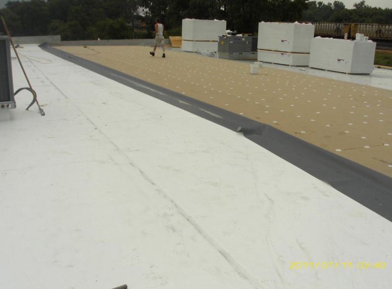 Flat rooftop with white and tan roofing sections, equipment, and a person in the distance
