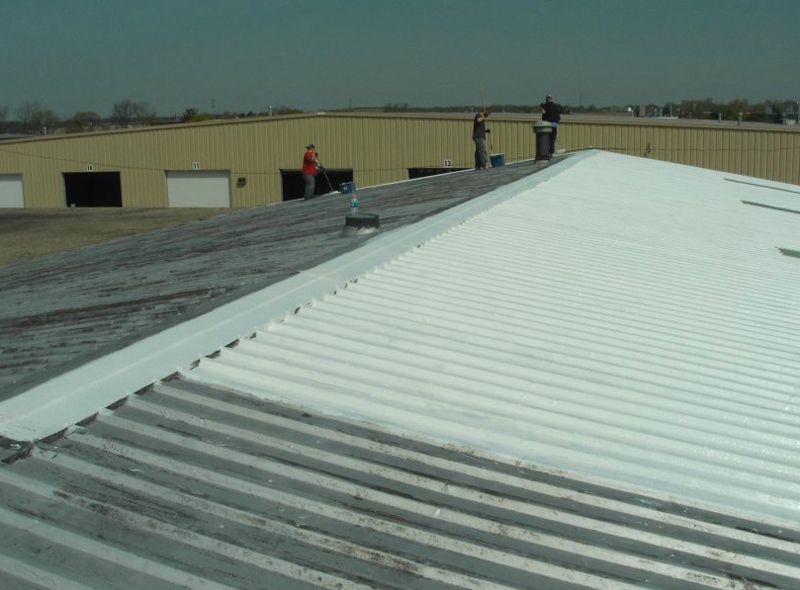 Rooftop with white metal panels and two workers in the distance under a clear sky