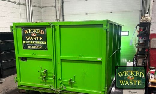 Bright green Wicked Waste dumpster inside a warehouse, with a matching sign nearby.