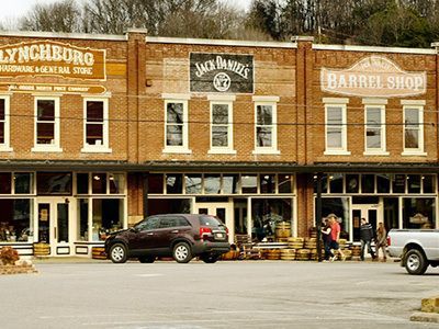 Small-town storefronts with brick facades, including Jack Daniel’s and Barrel Shop, with parked cars in front.