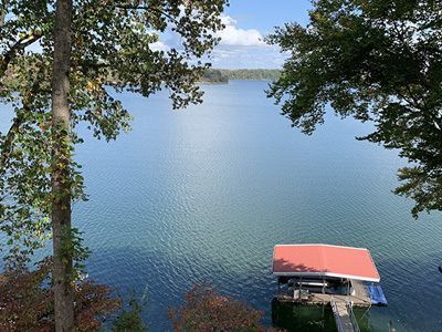 Lake view framed by trees, with a small dock and red-roofed boathouse in the lower right.