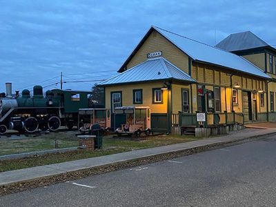 Vintage train station with a steam locomotive at dusk, yellow building with lit windows and blue roof