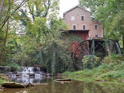 Watermill beside a small waterfall and stream, surrounded by trees and greenery