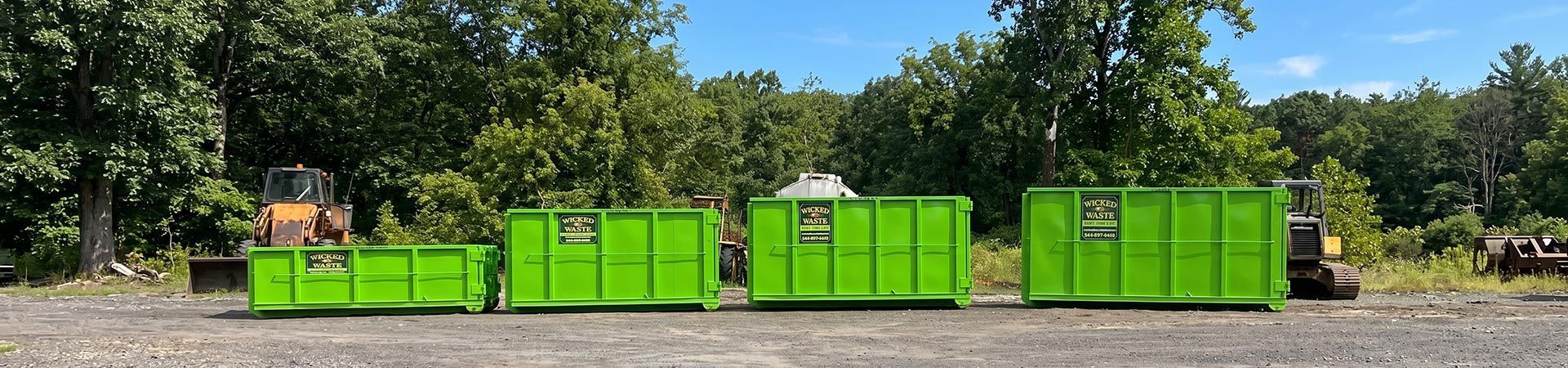 Bright green dumpsters and bins lined up along a street in front of trees and houses