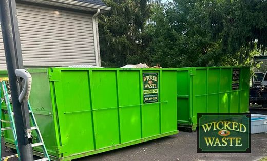 Bright green waste dumpster beside a house, with a “Wicked Waste” sign on the front.