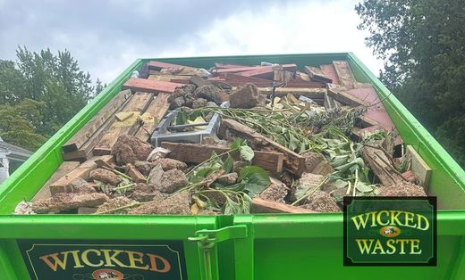 Green dumpster filled with construction debris and rubble under an overcast sky