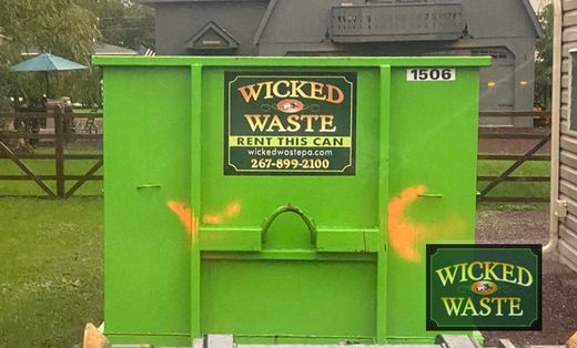 Bright green dumpster labeled “Wicked Waste” in a yard near a house
