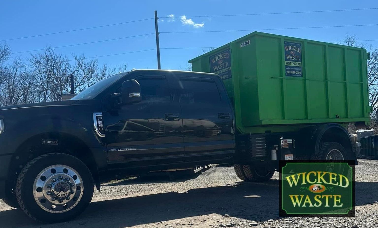 Black pickup truck hauling a green dumpster marked “Wicked Waste” on a sunny roadside