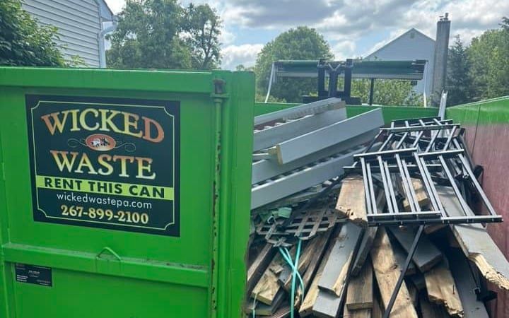 Green Wicked Waste dumpster beside a pile of construction debris and metal scrap outdoors