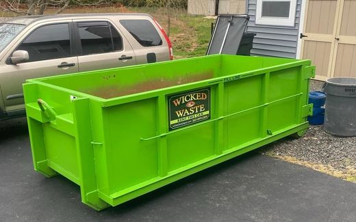 Bright green dumpster in a parking lot beside a tan SUV and a building.