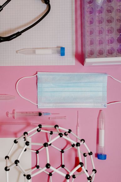 Artículos médicos sobre fondo rosa: mascarilla, tubos de ensayo, guantes y modelo molecular.