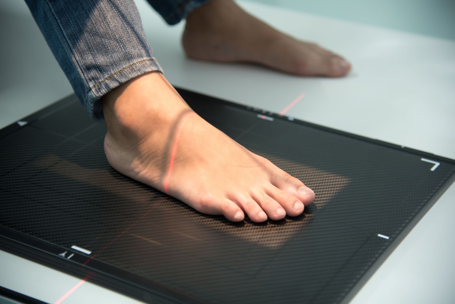 Foot on an X-ray plate, positioned for imaging. Pink laser lines guide the foot placement.