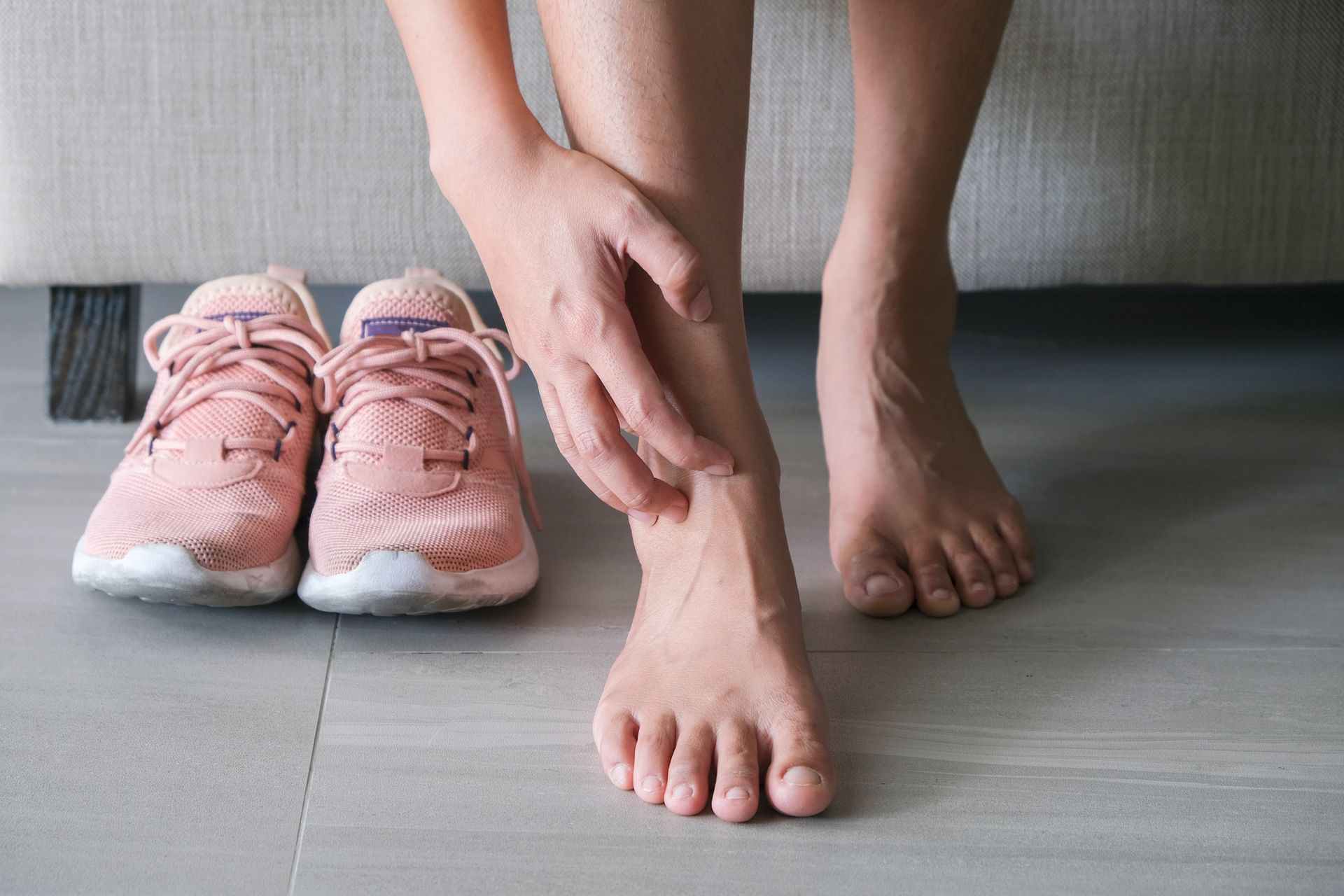 Person touching their ankle, sneakers beside them.