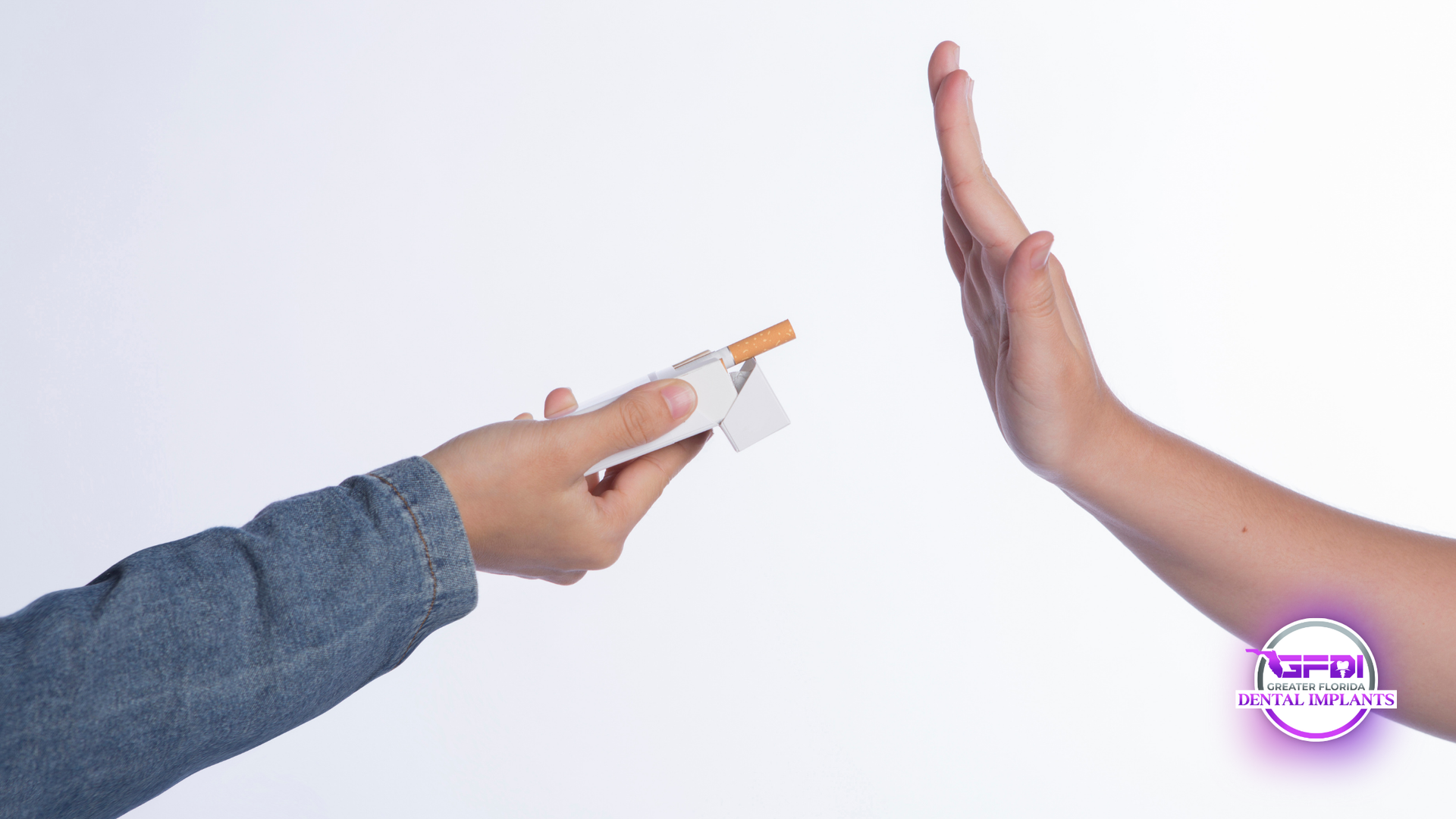 Person refusing cigarette offered from another hand. White background, denim sleeve.
