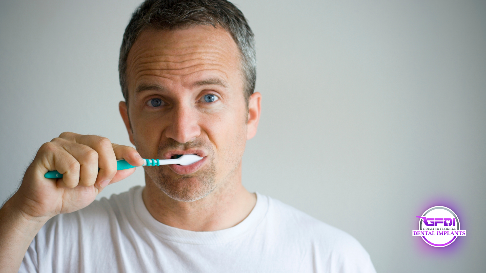Man brushing teeth with a blue toothbrush in front of a white background.