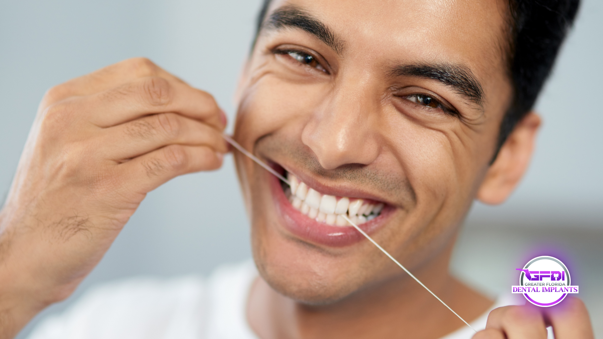 Man flossing teeth with a smile, holding dental floss close to his mouth.
