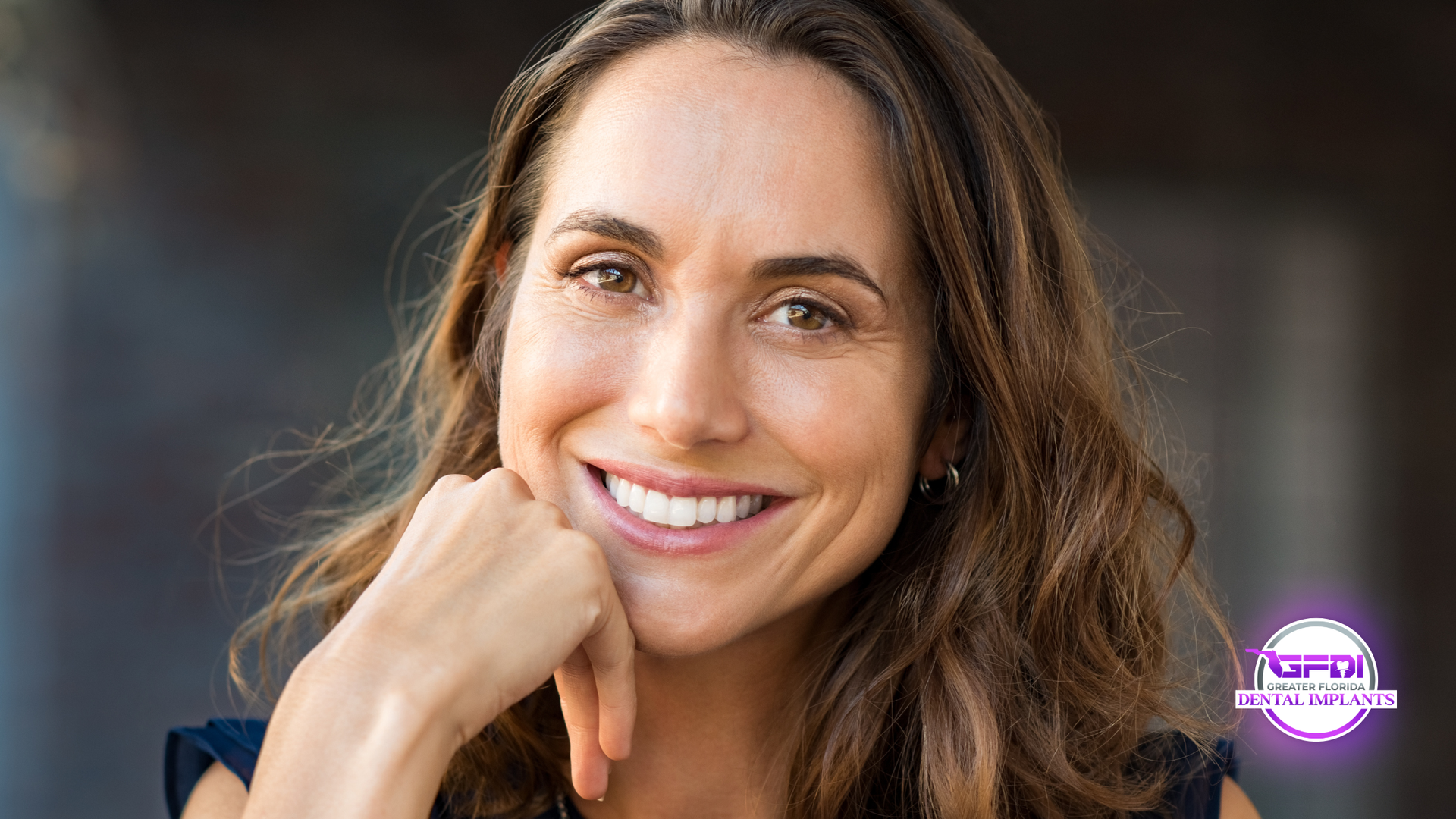 Smiling woman looking upward against a neutral background with a small purple logo in the corner