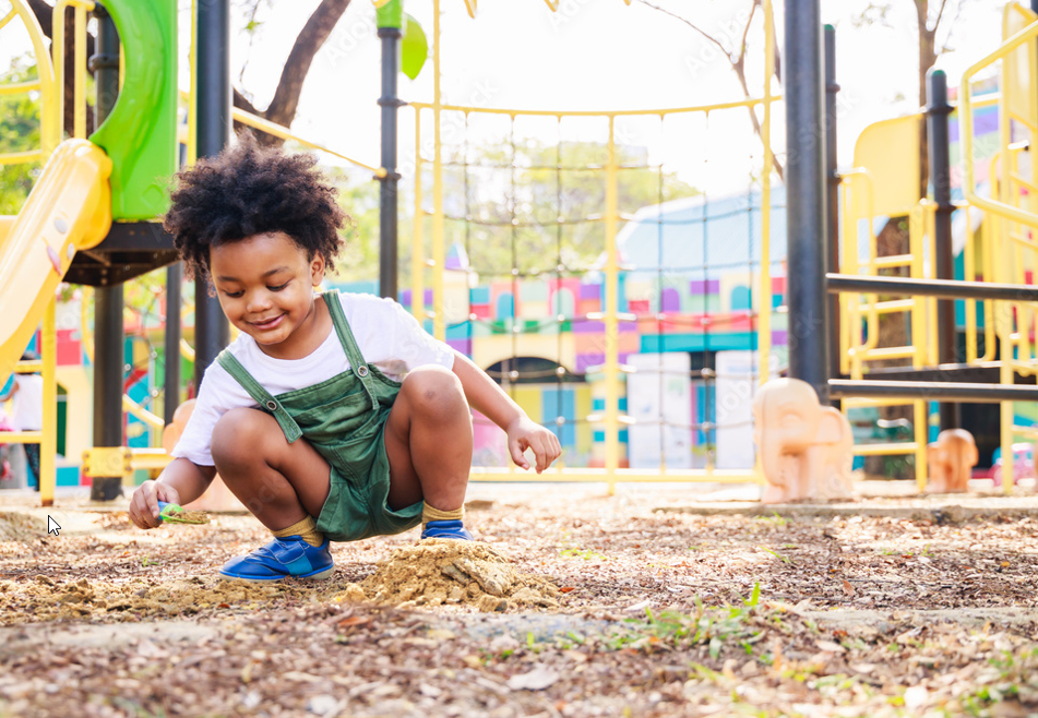Young child crouching, playing with dirt on a playground.