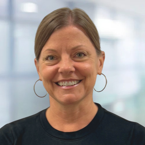 Smiling woman with hoop earrings in a dark shirt against a blurred office background