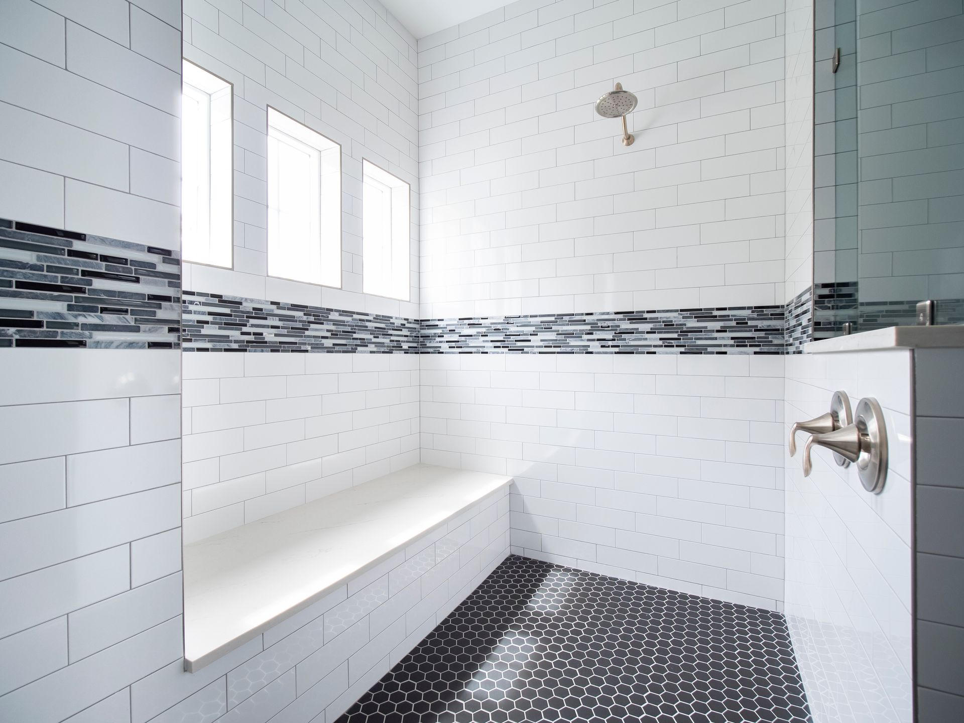 White tiled bathroom with a built-in bench, shower head, and black hexagon tiled floor.