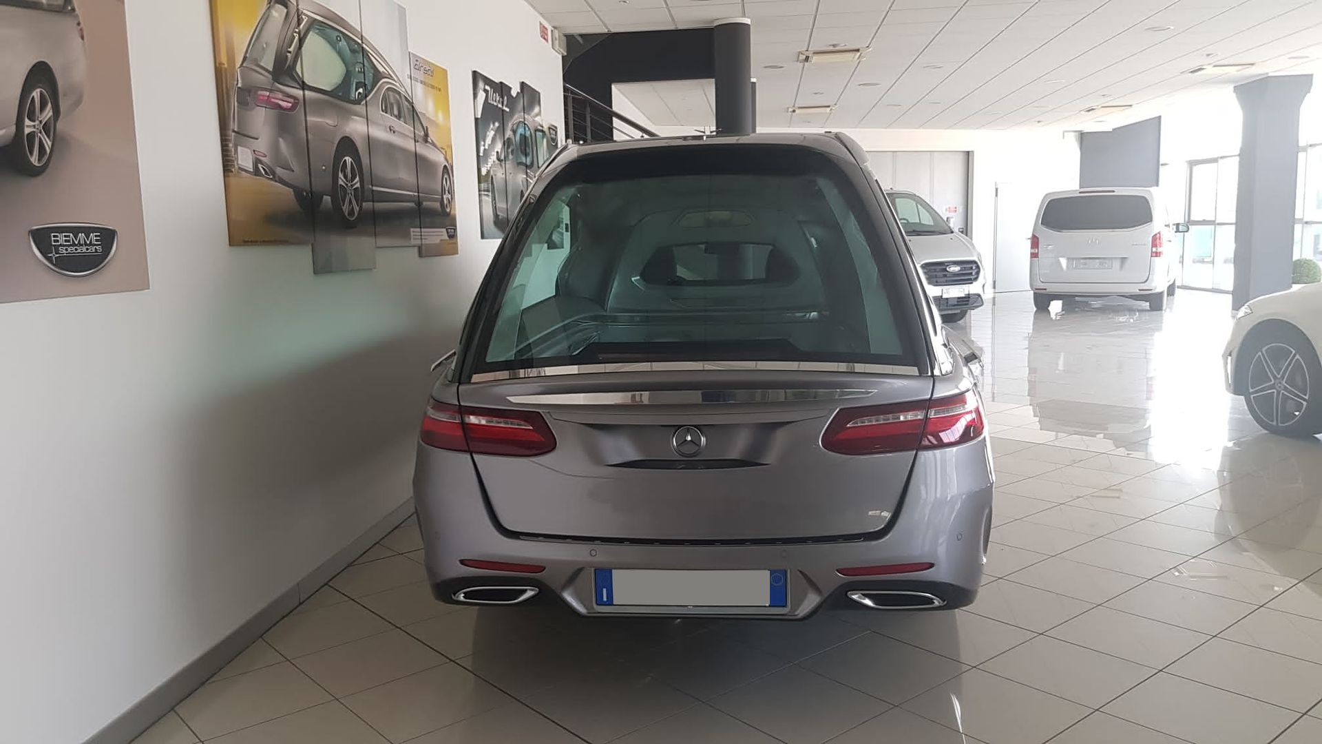 Un carro funebre argentato parcheggiato all'interno dello showroom di una concessionaria.