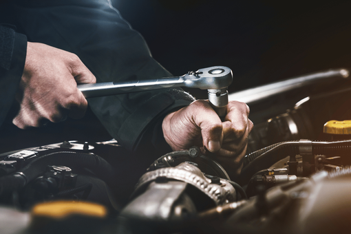 Mechanic using a ratchet wrench to repair a car engine in a dim garage