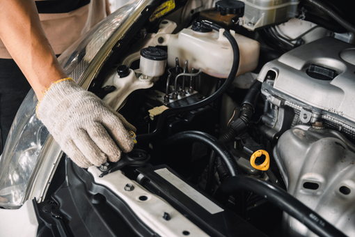 Gloved hand working under a car hood beside the engine and fluid reservoirs