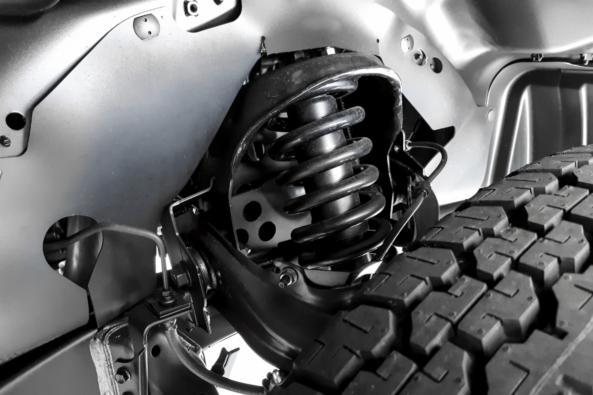 Close-up of a vehicle suspension spring beside an off-road tire and wheel well