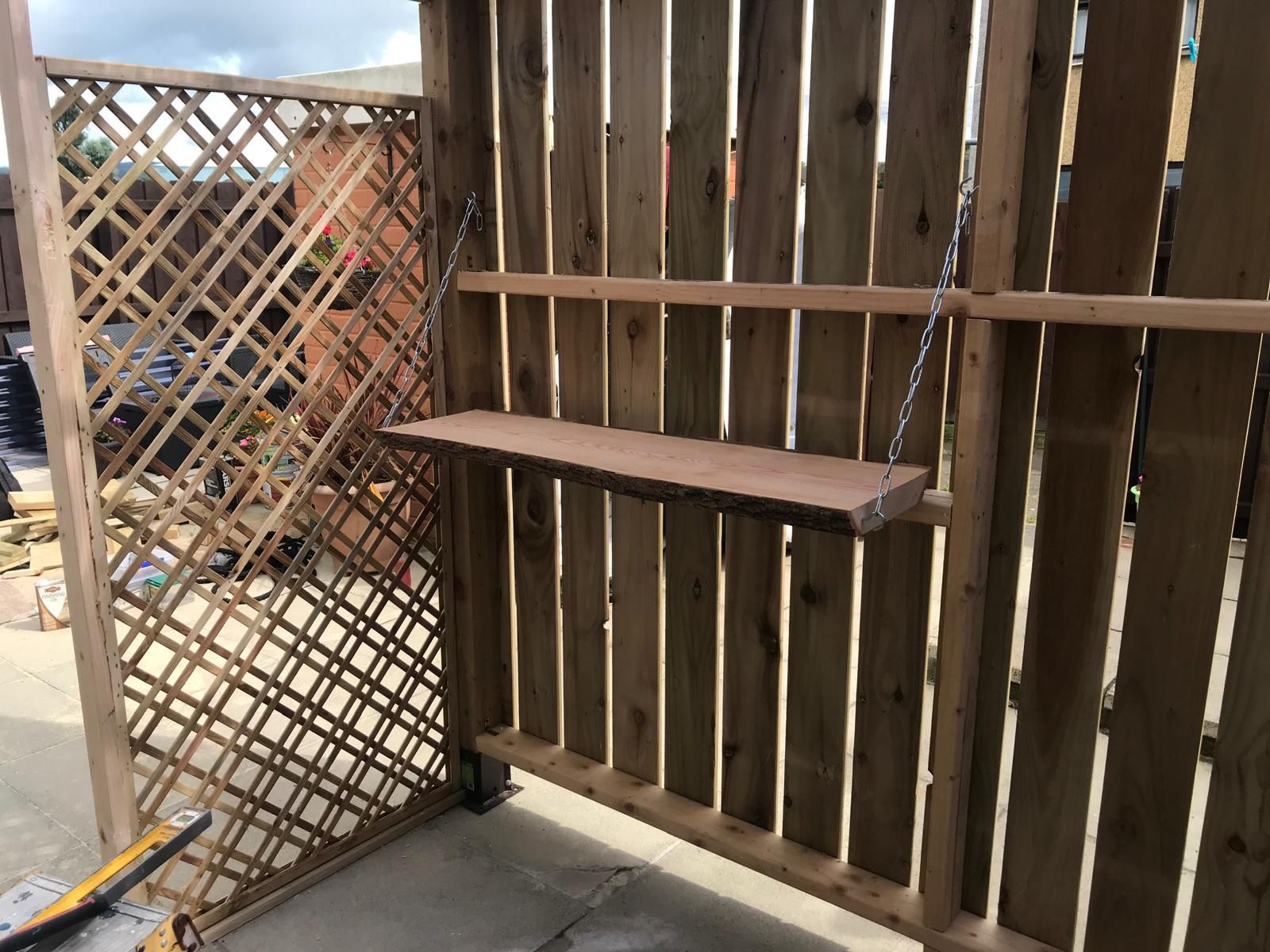 A wooden shelf is attached to a wooden fence.