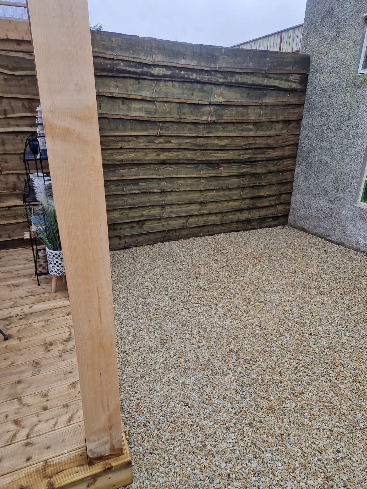 A wooden fence surrounds a gravel area in a backyard.