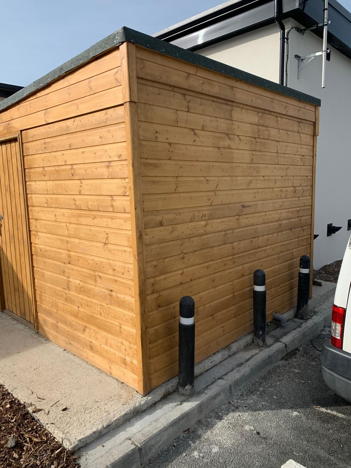 A wooden shed is sitting next to a white van in a parking lot.
