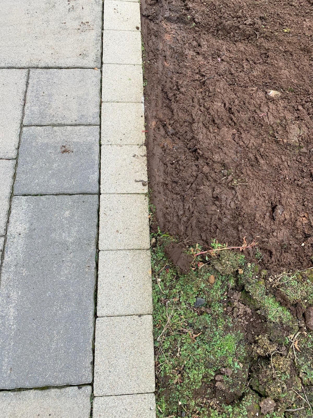A sidewalk and a dirt field are next to each other.