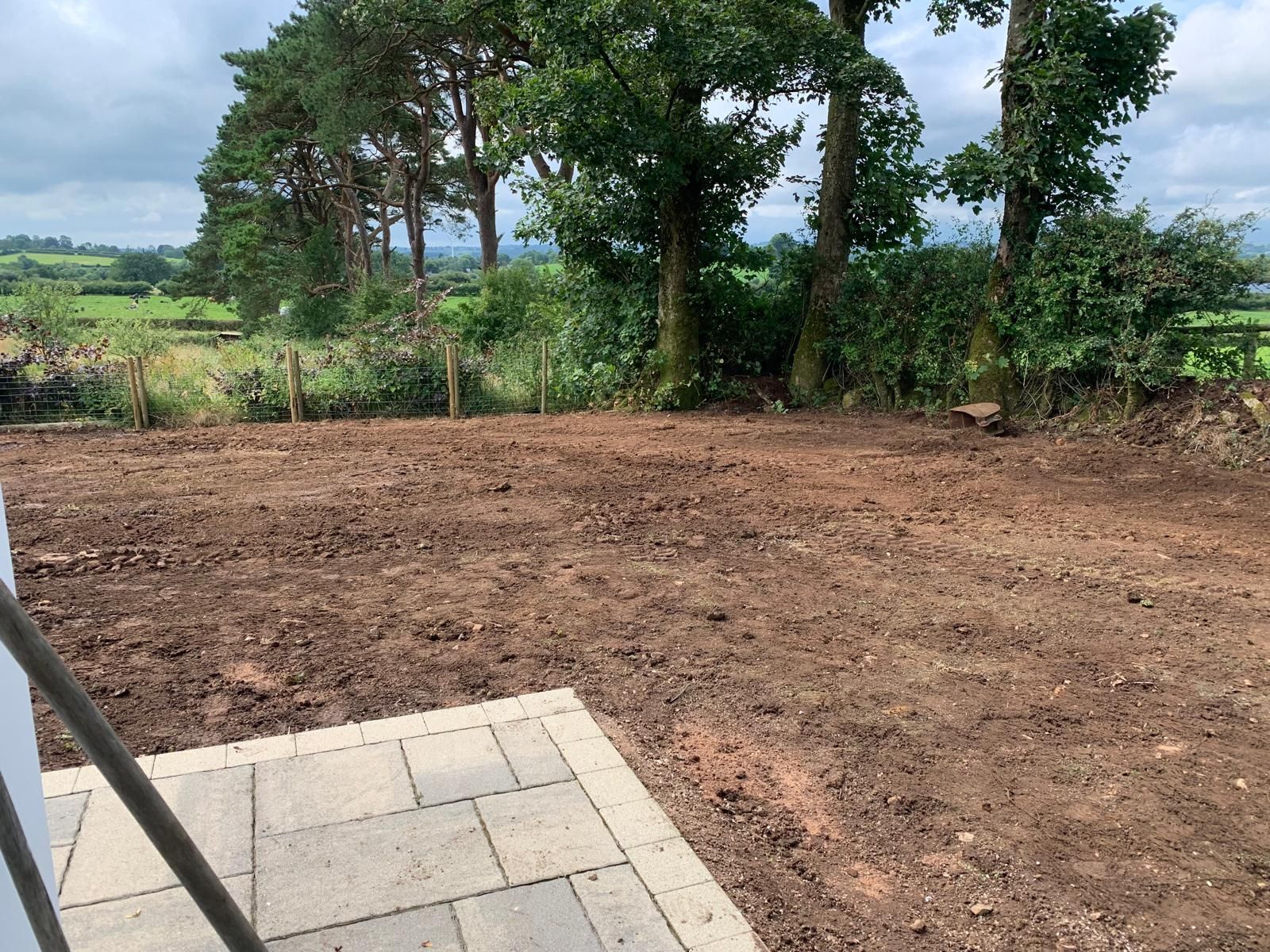 A dirt field with trees in the background and a patio in the foreground.