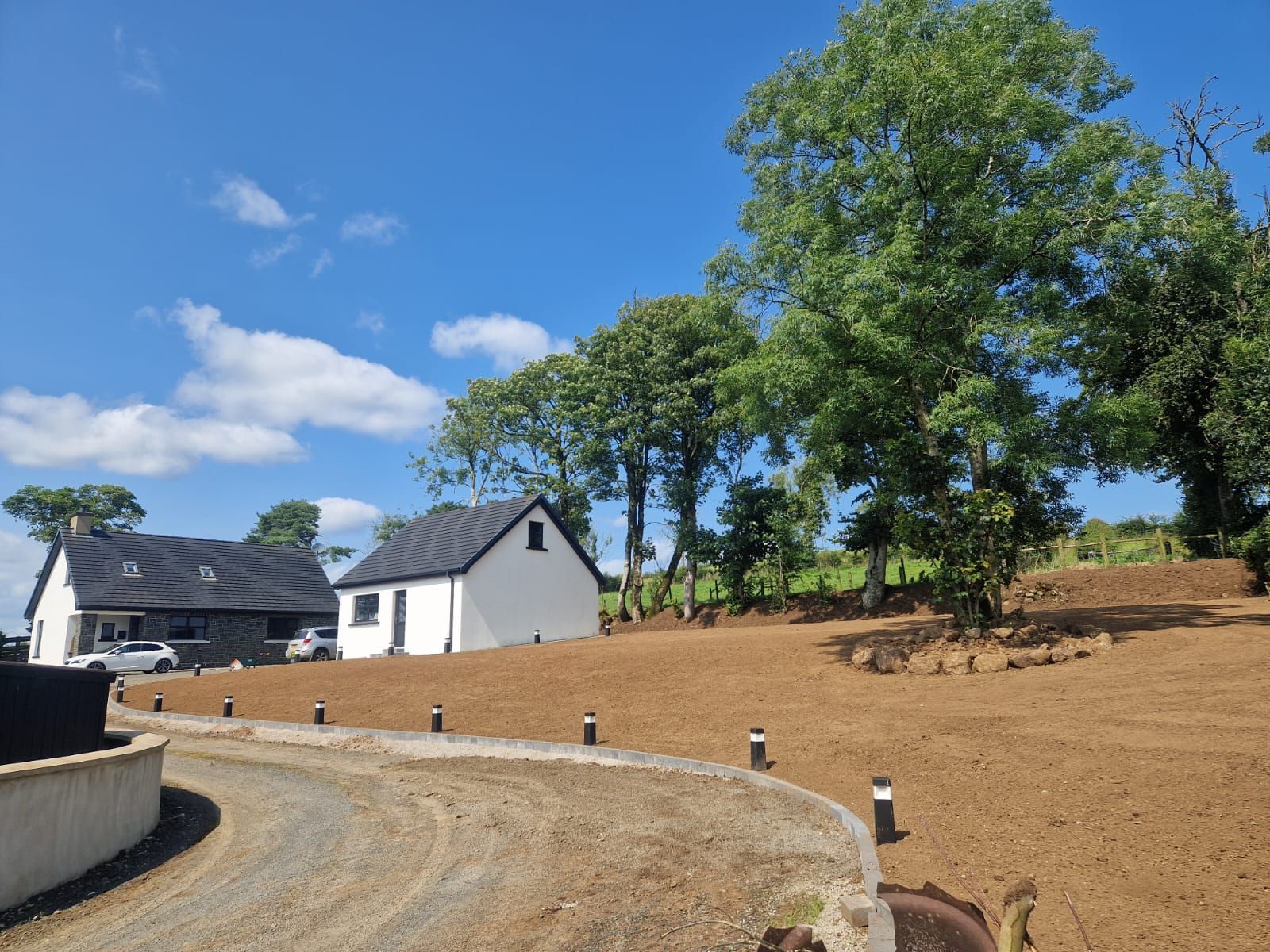 A white house with a black roof is surrounded by trees and dirt.