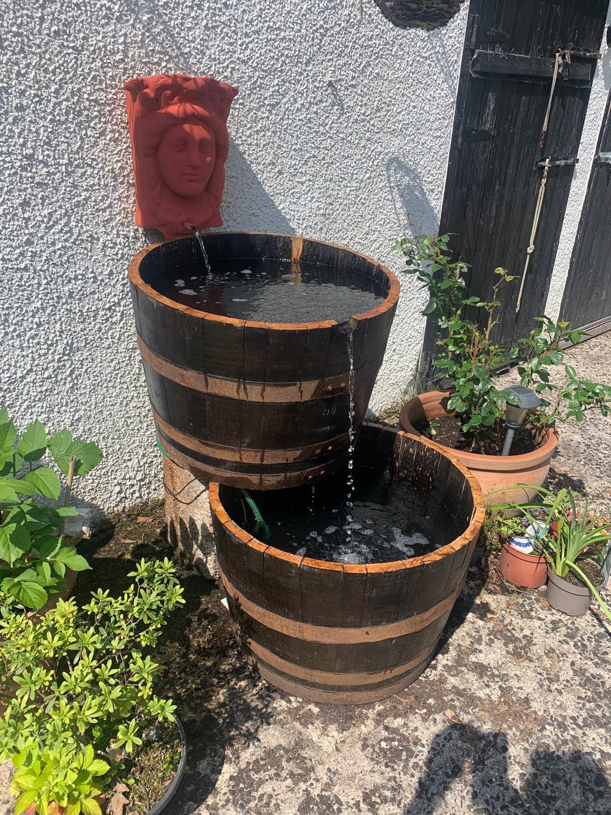A water fountain made out of wooden barrels and potted plants.