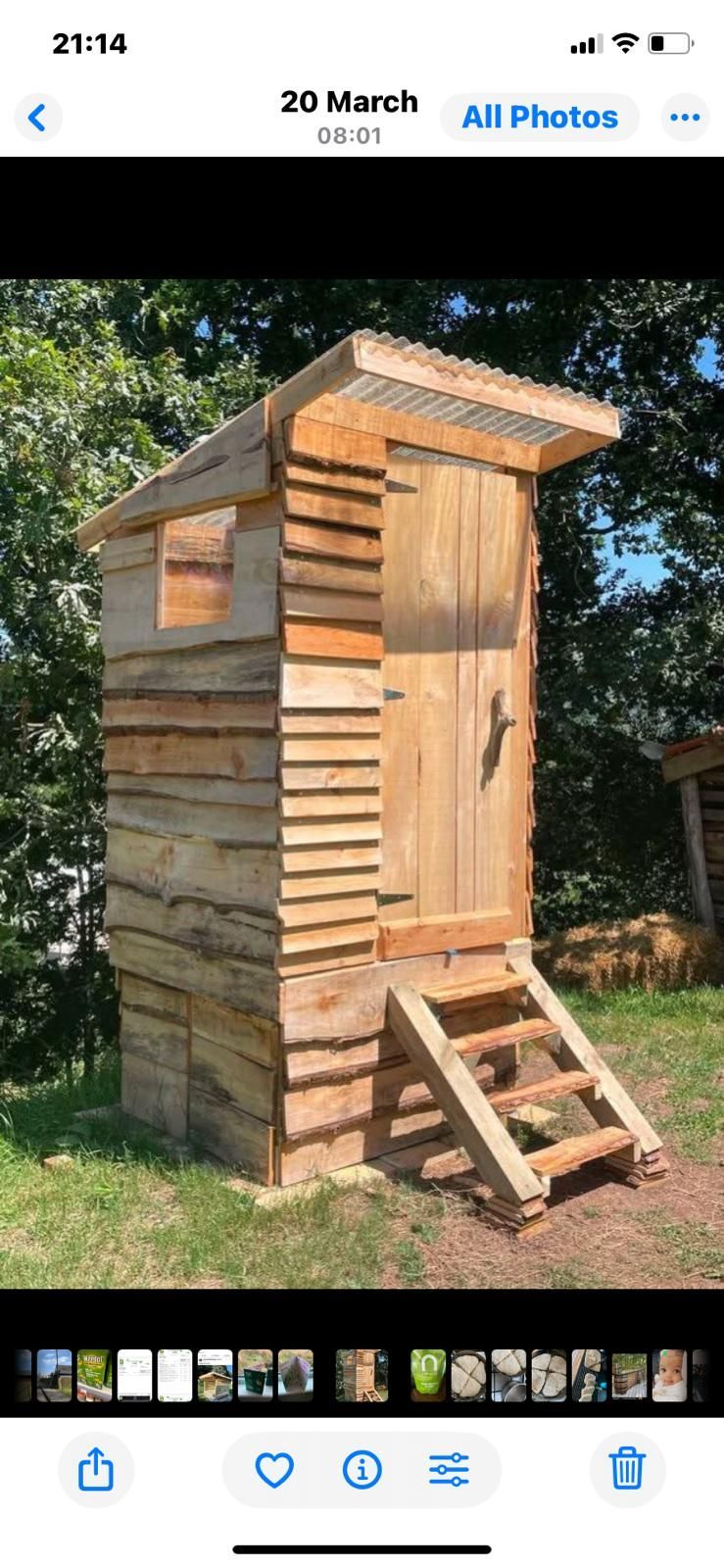 A wooden outhouse with stairs leading up to it is sitting on top of a lush green field.