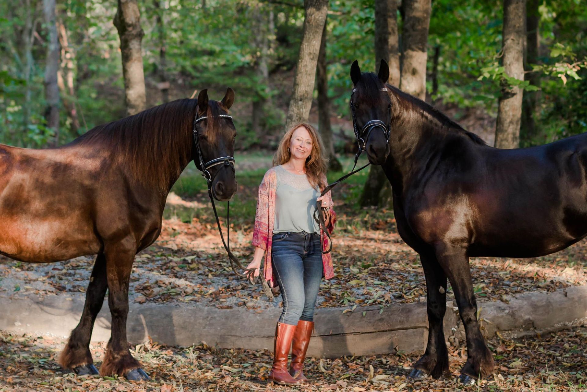A woman is standing next to two horses in the woods.